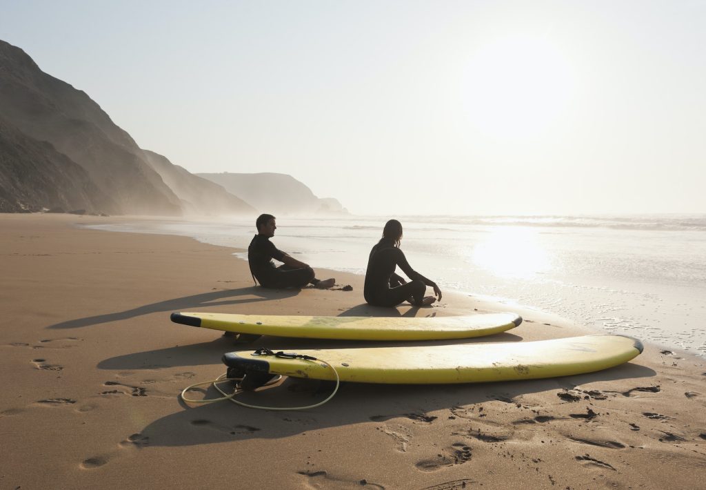 Portugal, Couple sitting on beach by surfboard