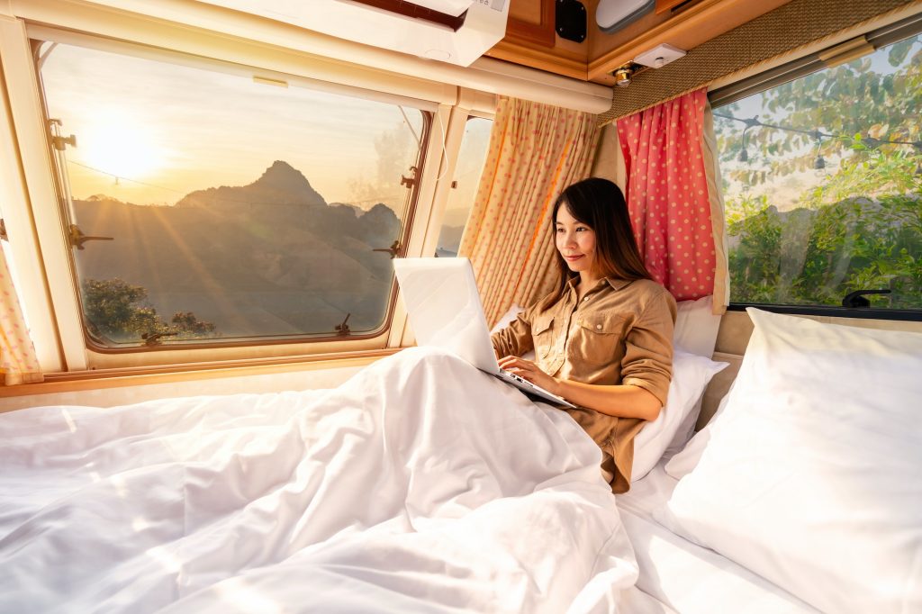 Young woman traveler laying in camper van and using laptop